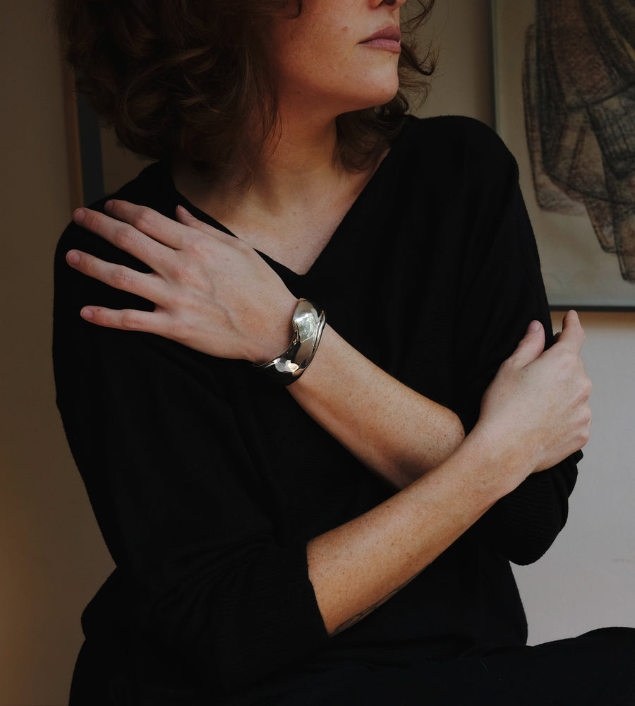 Woman in a dark room with a warm light source, wearing a black top with a silver cuff