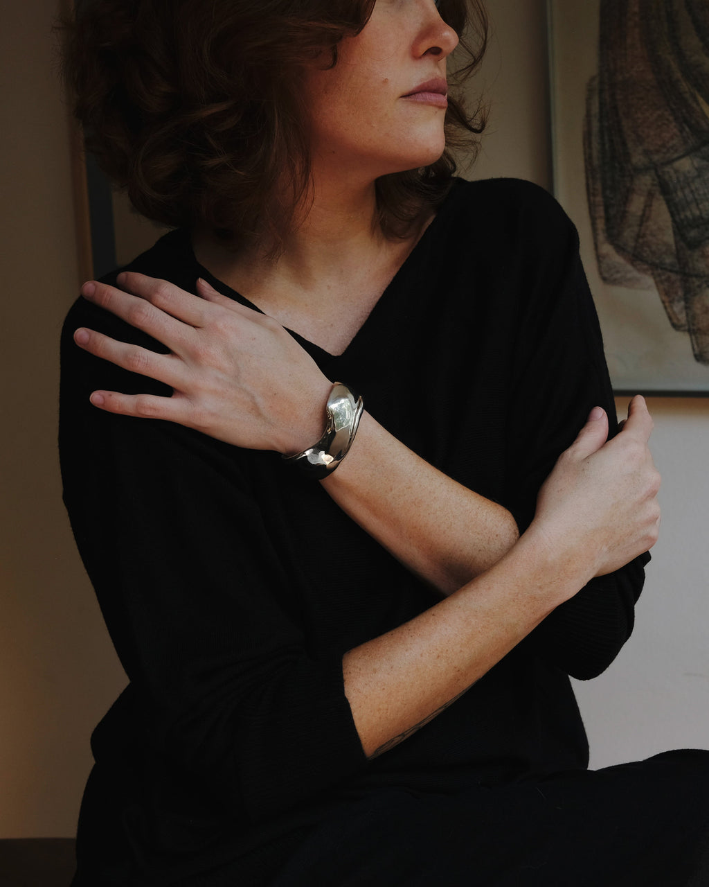 Woman in a dark room with a warm light source, wearing a black top with a silver cuff