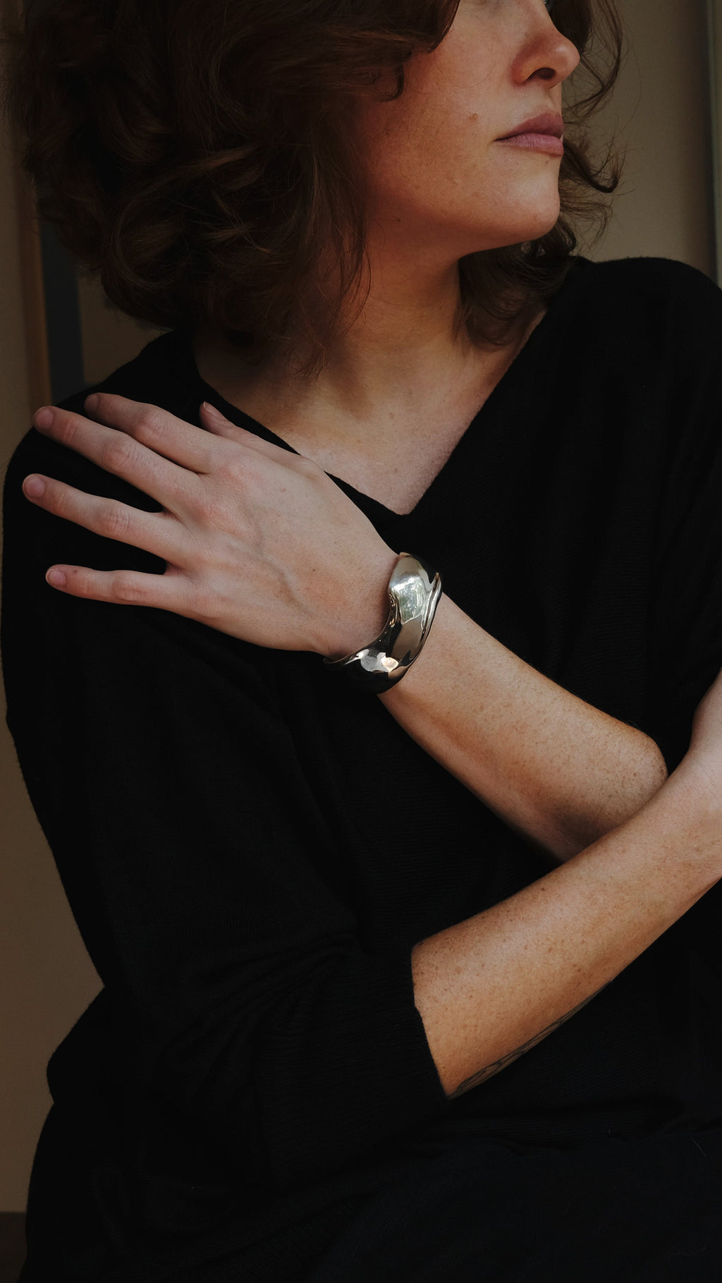 Woman in a dark room with a warm light source, wearing a black top with a silver cuff bracelet