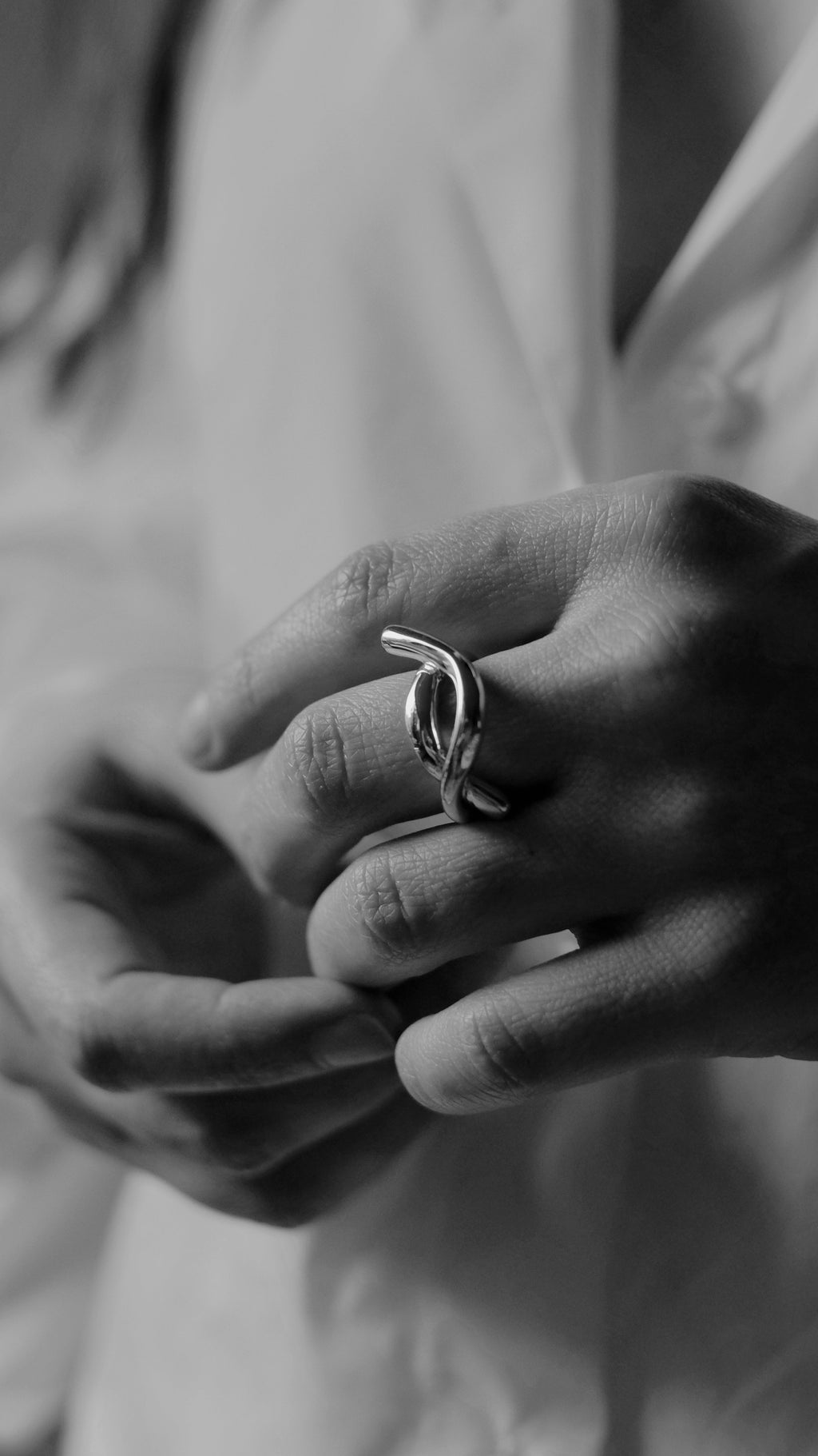 Close-up of hands with a ring, wearing a light-colored shirt.