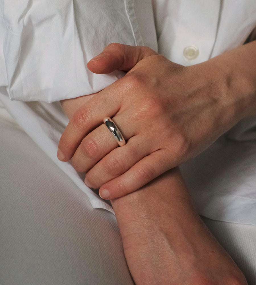 Close-up of two hands clasped together, wearing a ring, with a blurred background.