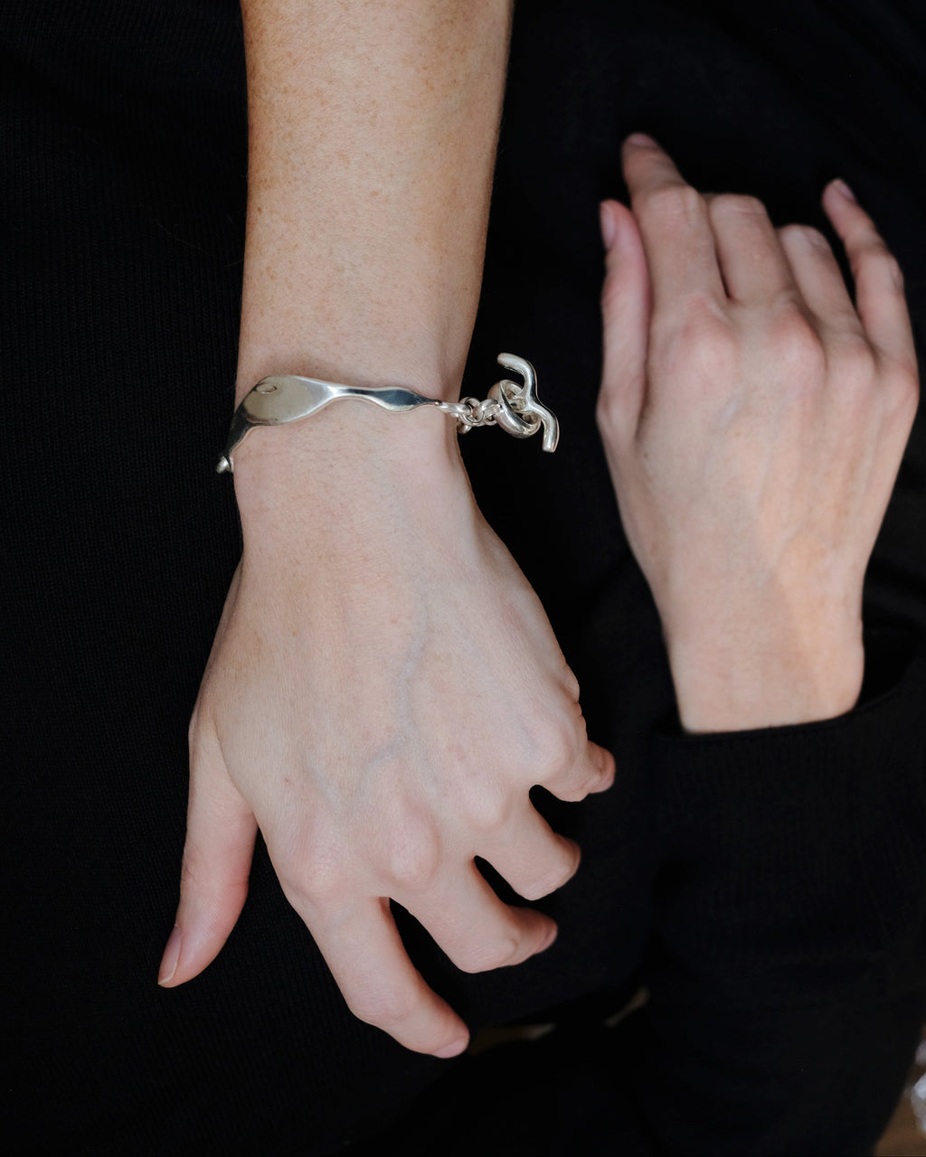 Person wearing a silver bracelet with a unique design on a dark background