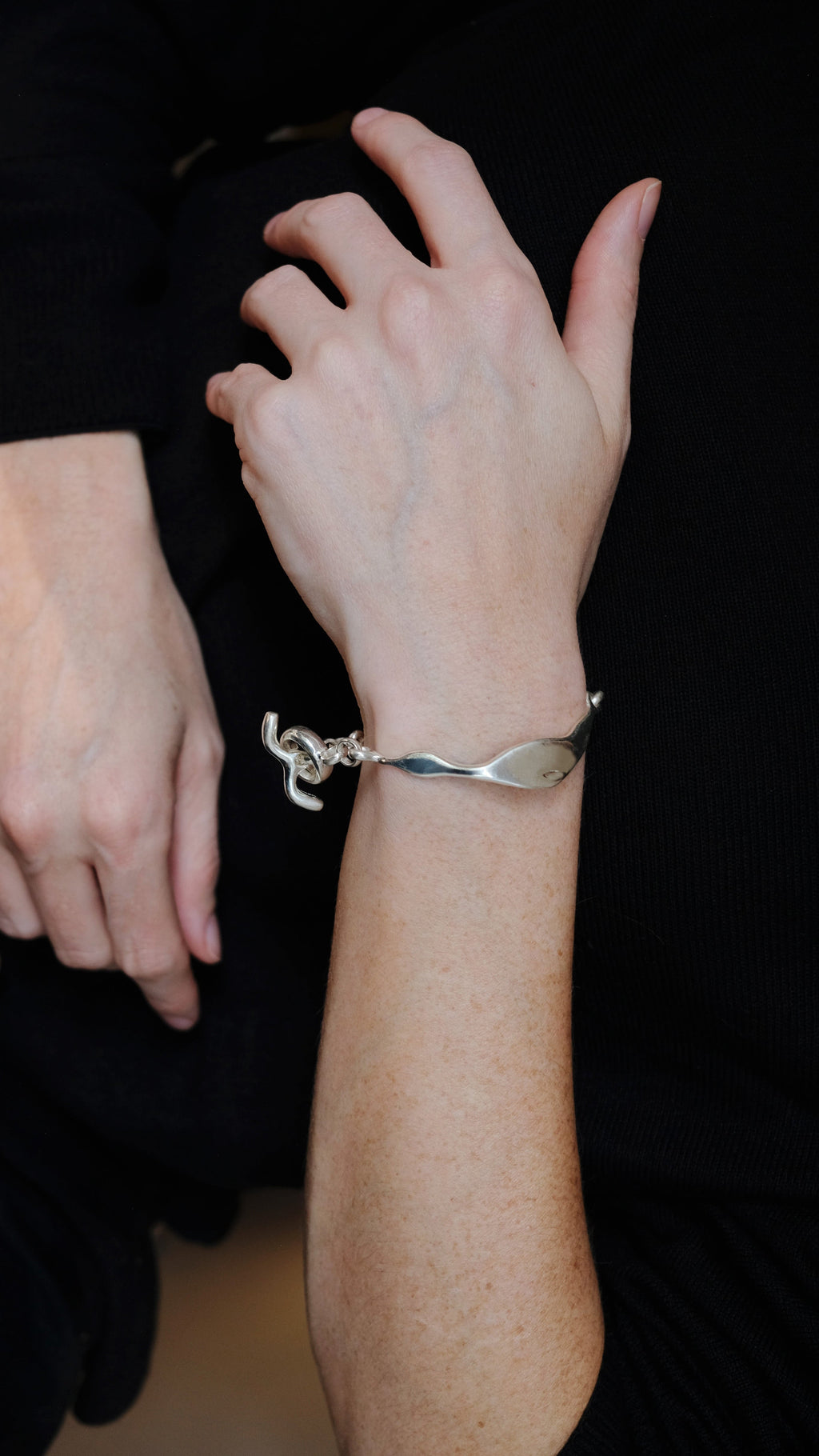 Person wearing a silver bracelet with a unique design on a dark background