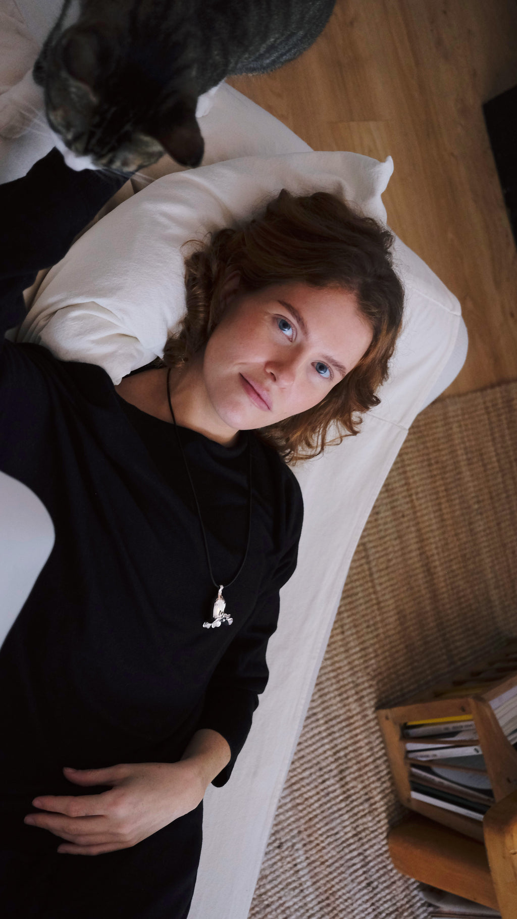 Woman lying on a couch with a cat next to her in a cozy living room wearing a flower silver necklace