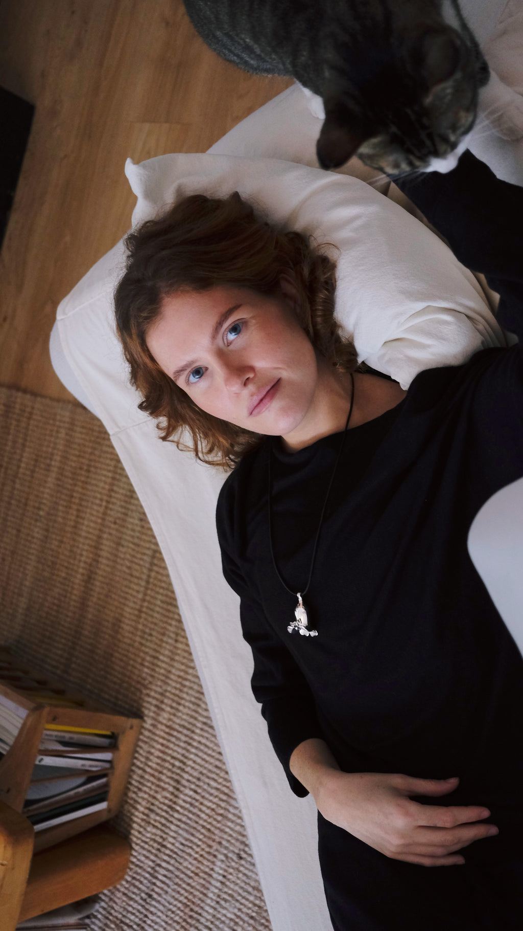 Woman lying on a couch with a cat next to her in a cozy living room wearing a flower silver necklace