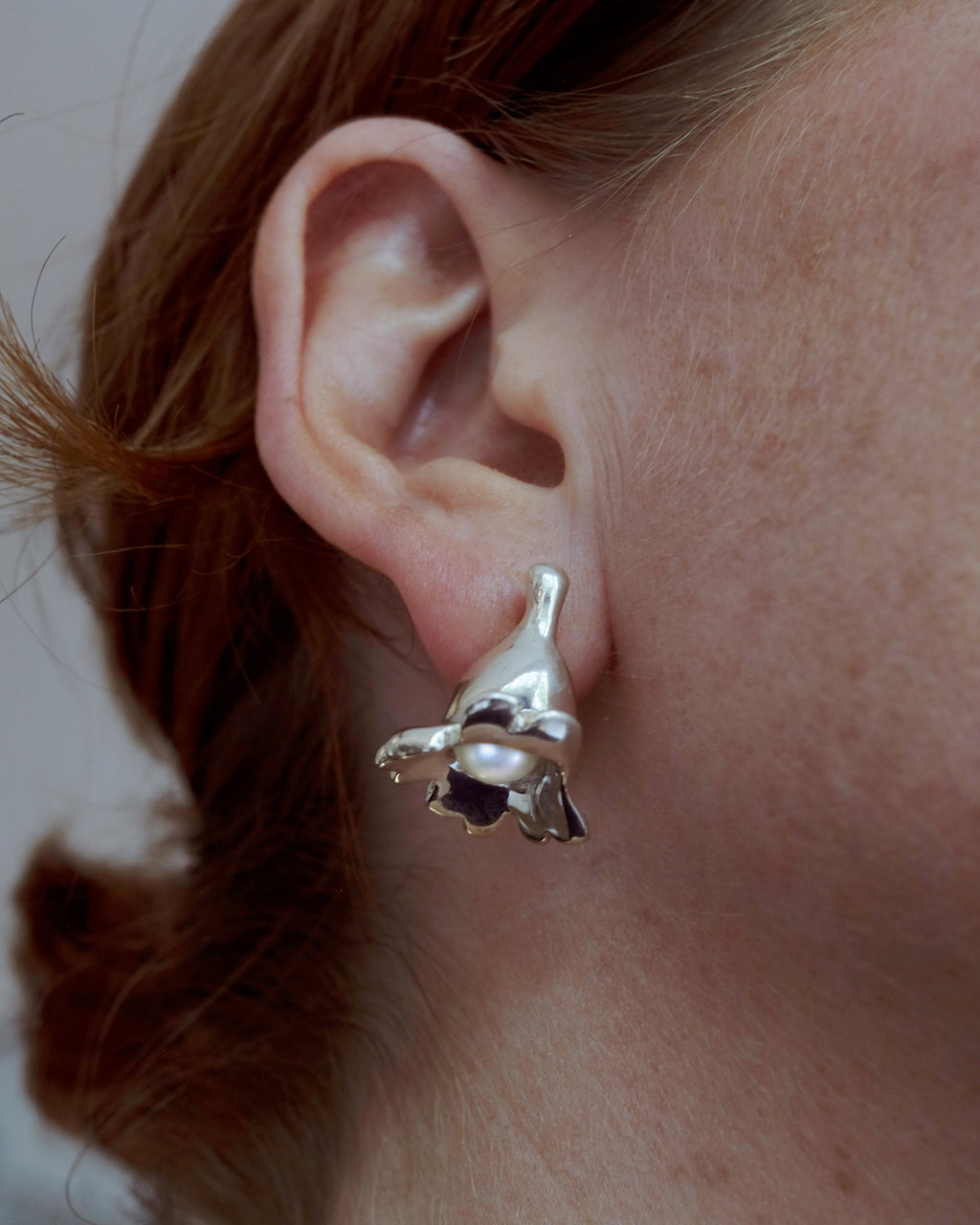 Close-up of a person wearing a silver earring with a pearl