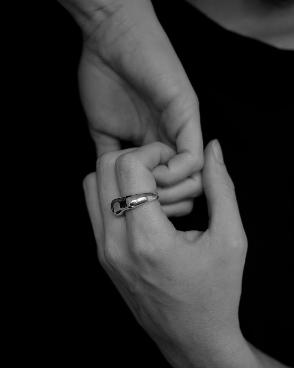 Black and white photo of two hands holding each other with a ring on one finger.